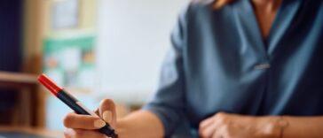 Close up of a teacher's hand grading tests of her students in the classroom.