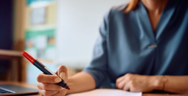 Close up of a teacher's hand grading tests of her students in the classroom.