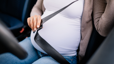 pregnant woman buckling up in driver's seat